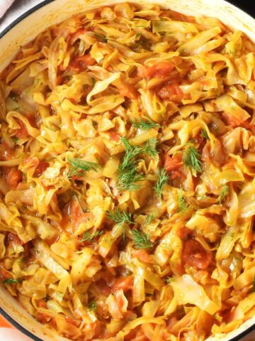 Top down view of stewed cabbage and tomatoes in large white pan.